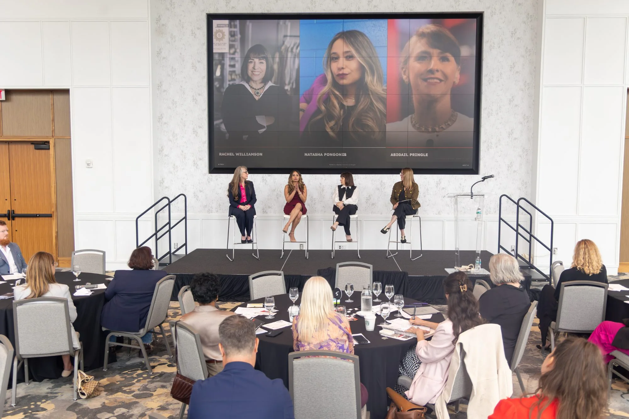 Rachel Williamson seated on stage with fellow panelists in front of a seated audience